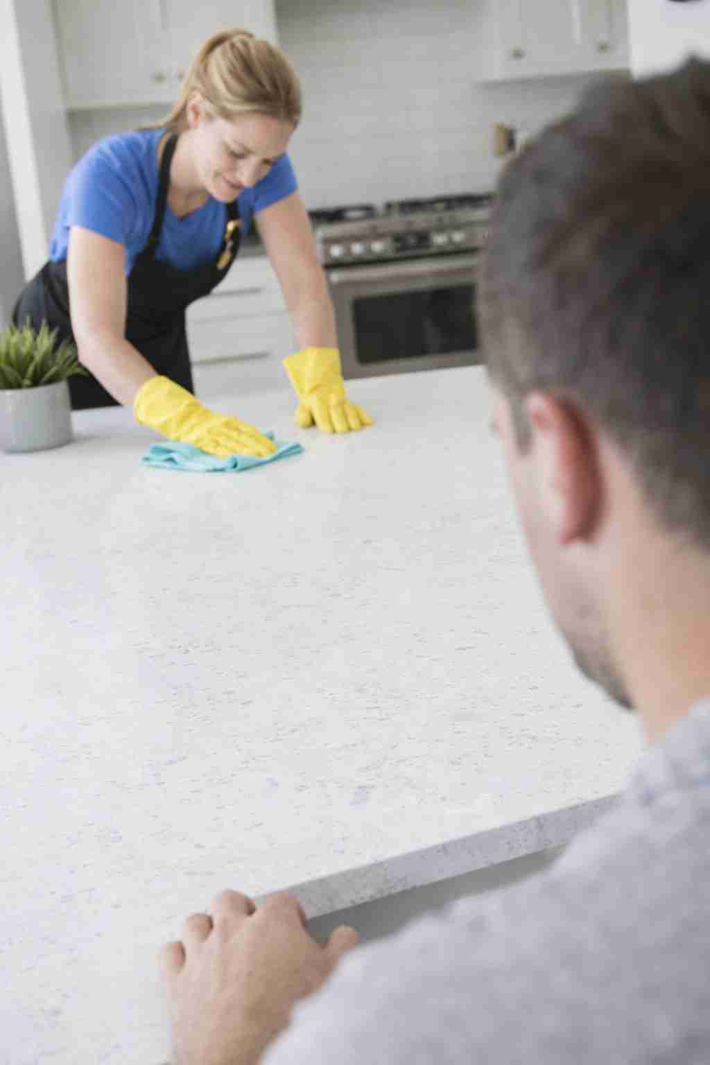 Professional house cleaner wiping down kitchen counter while homeowner compares Homeaglow and The CoBuilders services online